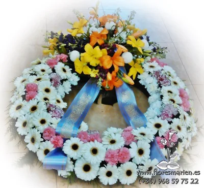 Funeral wreath of white gerberas and pink carnations with a spray of lilies and a blue ribbon